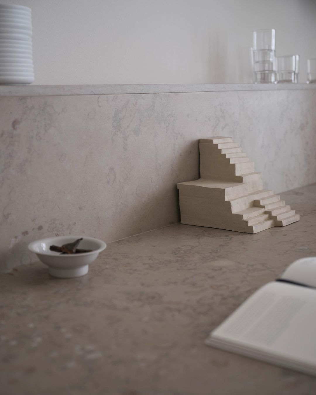 Minimalist photo of a small architectural model of stairs on a countertop, featuring neutral tones and a simple, artistic composition.