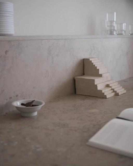 Minimalist photo of a small architectural model of stairs on a countertop, featuring neutral tones and a simple, artistic composition.