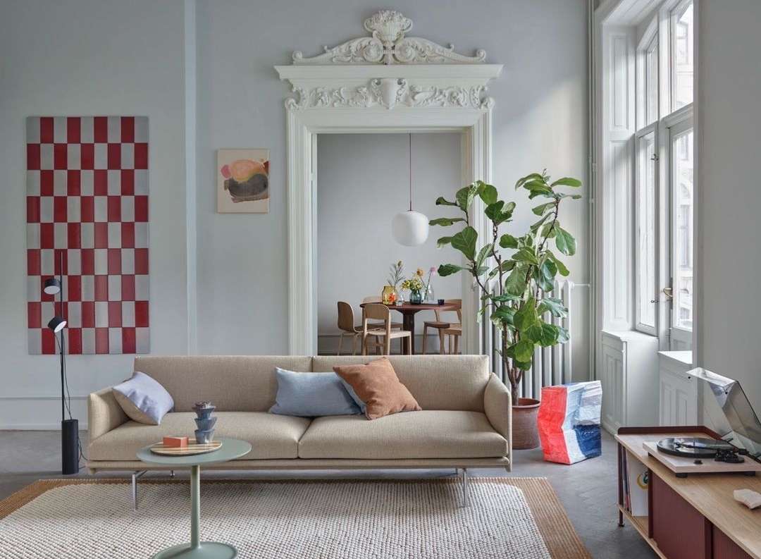 Living room interior with a beige sofa, round coffee table, indoor plants, and a dining table with chairs in the background.