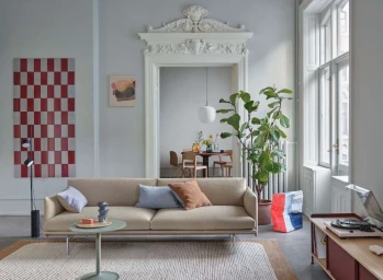 Beige modern sofa in an apartment living room with light grey walls, a red patterned wall panel, and an ornate white doorway.