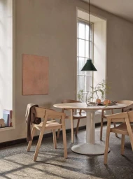 Minimalist dining room interior featuring a round wooden table, chairs, pendant lamp, and neutral plaster walls by photographer Petra Bindel