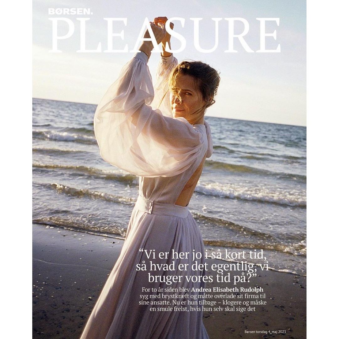Fashion magazine cover featuring an adult woman in a white dress posing on a beach with waves.  Borsen Pleasure magazine cover.