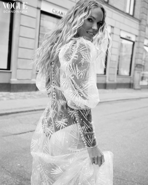 Black and white portrait of a woman in a sheer patterned dress on a city street near Chanel store, fashion editorial for Vogue Scandinavia.