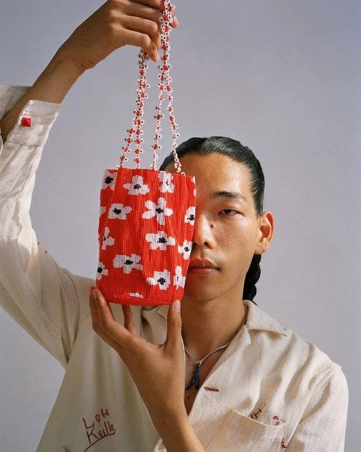 Person holds a red beaded purse with white flower pattern against a plain background in a studio shot with soft, diffused lighting.