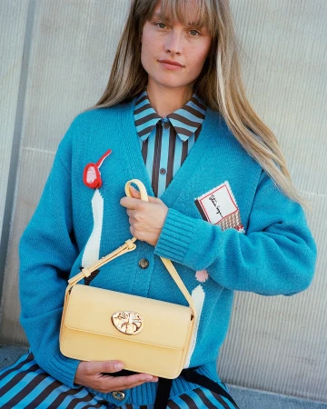 Woman wearing turquoise cardigan and striped shirt holding a yellow leather handbag by photographer Petra Kleis