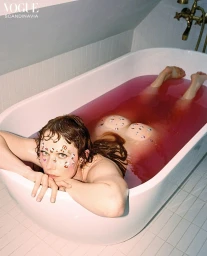 Woman in a pink-filled bathtub with decorative stickers on her face and body, photographed by Petra Kleis