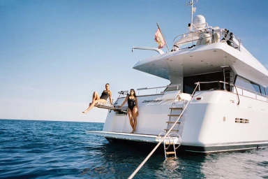Two women in black swimsuits posing on the stern platform of a white yacht on the ocean by Petra Kleis