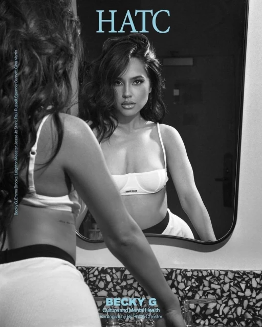 Brunette woman in a white bra and black and white shorts looks in a mirror in an indoor setting. The image is black and white.