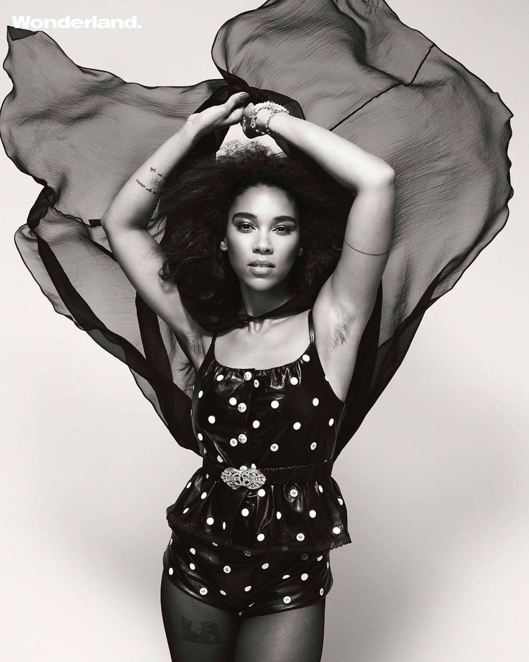 Woman with afro poses in polka-dot outfit and sheer cape for black-and-white portrait in photo studio with 'Wonderland' logo in the corner.
