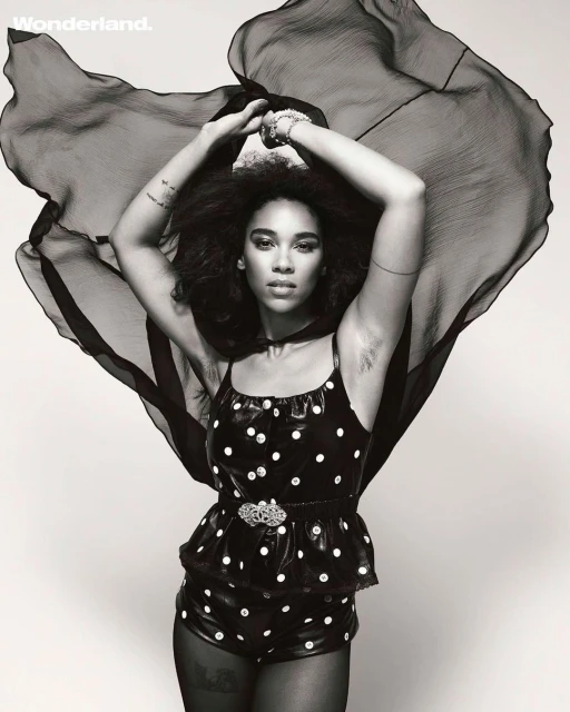 Woman with afro poses in polka-dot outfit and sheer cape for black-and-white portrait in photo studio with 'Wonderland' logo in the corner.