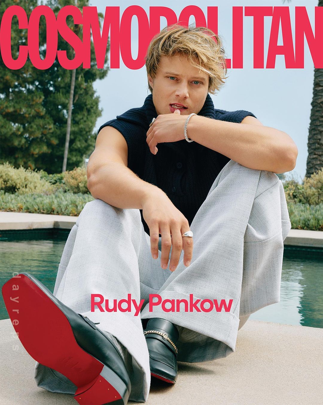 Cosmopolitan magazine cover featuring Rudy Pankow, casually posing outdoors by a pool, wearing a black sweater and grey pants, with loafers.