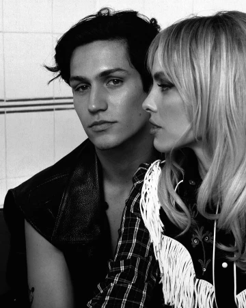 Monochrome portrait of a man with dark hair and a woman with bangs wearing patterned fringed apparel.