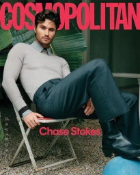 Chase Stokes seated outdoors on a folding chair wearing a light grey sweater and dark trousers photographed by Phil And Sara