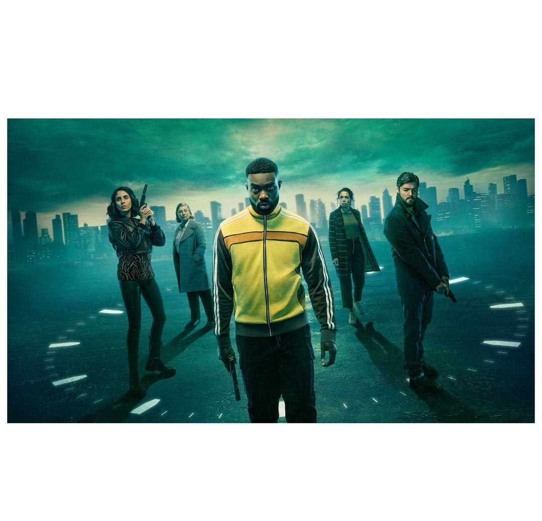 Group of diverse adults, armed with guns, stand on a street with a city skyline backdrop, suggesting a dramatic movie scene or promotional image.