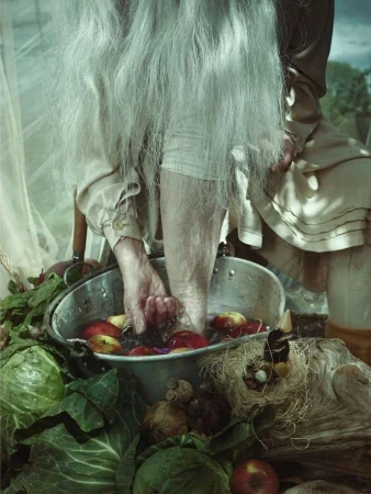 Elderly person washing feet in a basin of apples and vegetables, possibly outdoors. Focus on hands, feet, fruit, and surrounding items.