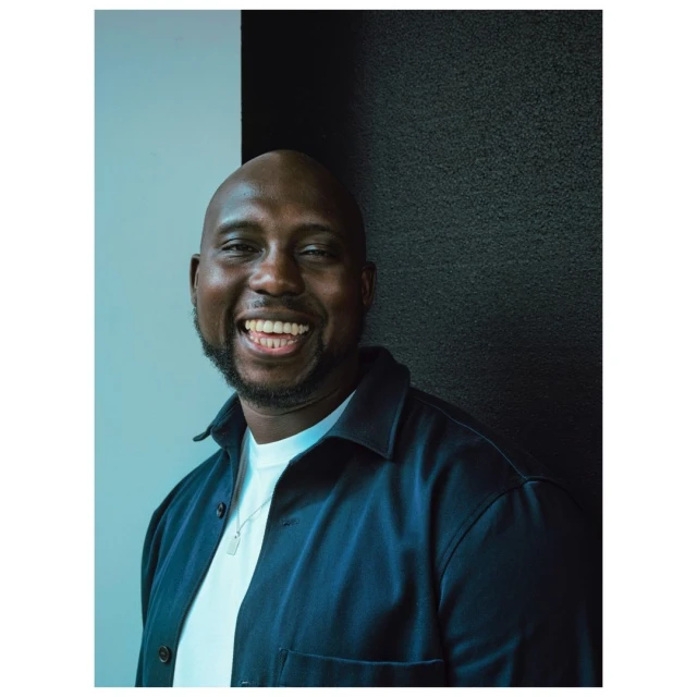 Smiling Black man portrait. African American male with beard wears dark blue shirt and white t-shirt with black and white wall background.