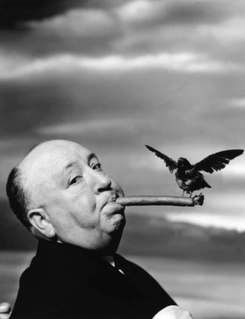 Black and white portrait of a man with a bird perched on a cigar, featuring a cloudy sky background; shot with a medium camera angle.