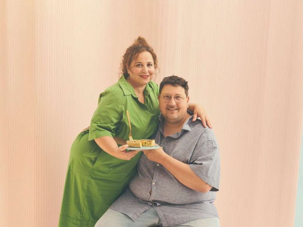 Man and woman holding a small tart on a plate against a pale pink background, photographed by Phil Fisk.