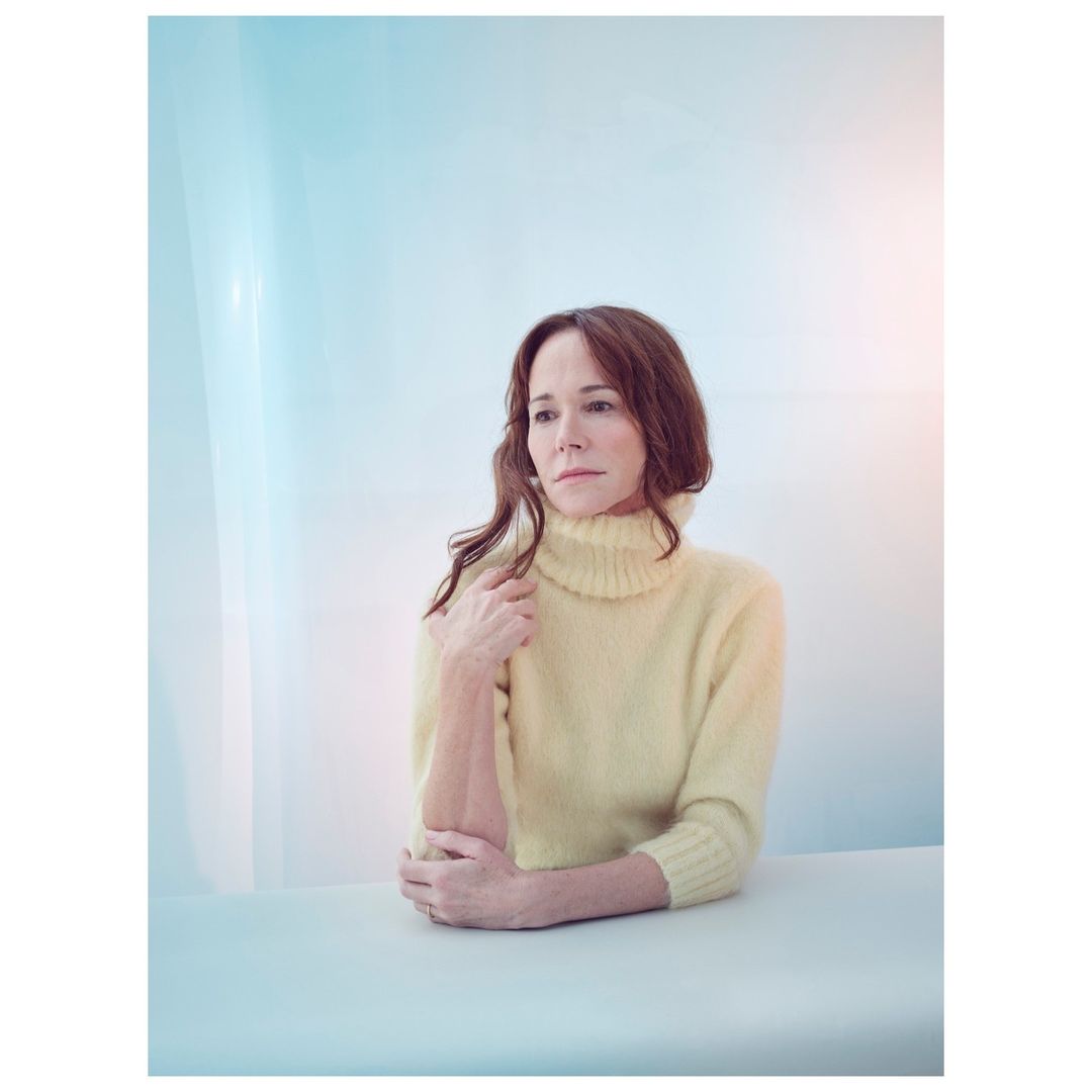 Portrait of a woman with shoulder-length brown hair wearing a yellow turtleneck sweater indoors with soft, diffused lighting. 