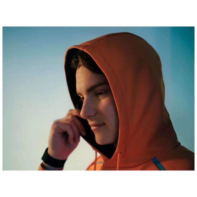 Portrait of a young adult in an orange hoodie looking toward the light, wearing a wristband, set against a gradated blue background.