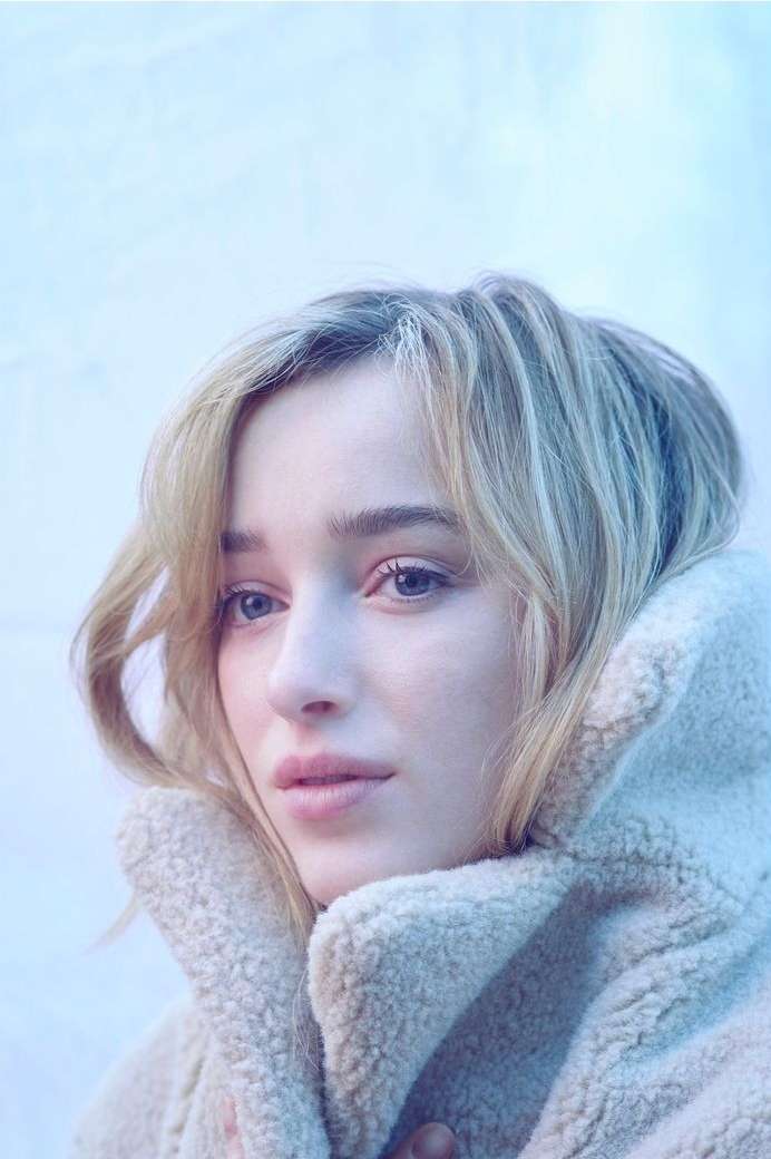 Portrait of an adult woman with light blonde hair wearing a cream-colored, sherpa-style jacket against a muted, blue-toned background.