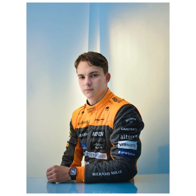 Portrait of a young adult in orange and black racing apparel in a studio, with a Richard Mille watch visible on his left wrist.