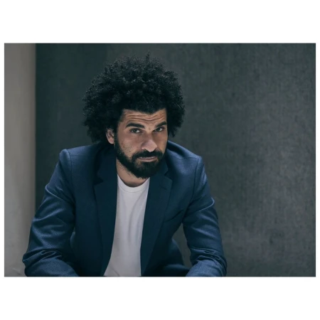 Portrait of a man with curly hair and a beard wearing a dark suit jacket and white t-shirt by photographer Phil Fisk