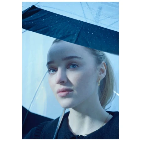 Portrait of a young woman under a transparent umbrella, looking thoughtfully to the side. The lighting is soft and diffused.
