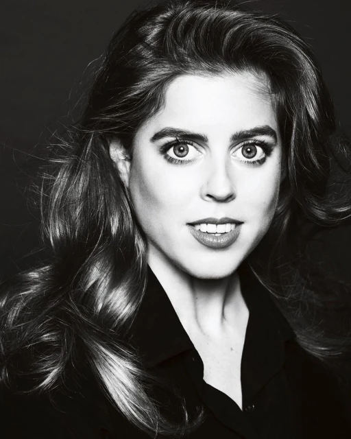 Headshot of a light-skinned adult woman with long wavy brown hair wearing a dark shirt, looking directly at the camera in a photo studio.