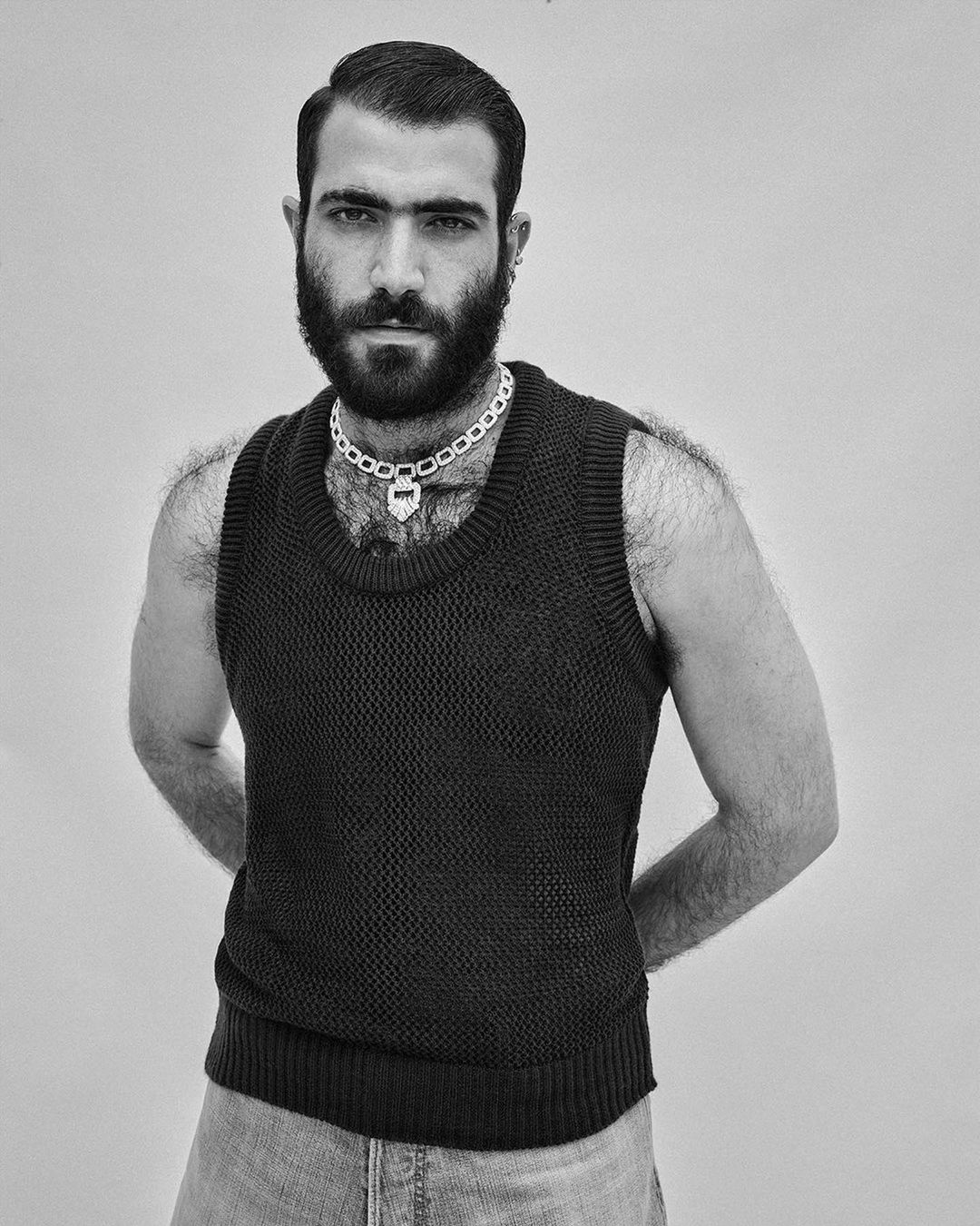 Portrait of an adult man with a beard and a knit vest, posing in a studio. The photo is in black and white, with a simple backdrop.