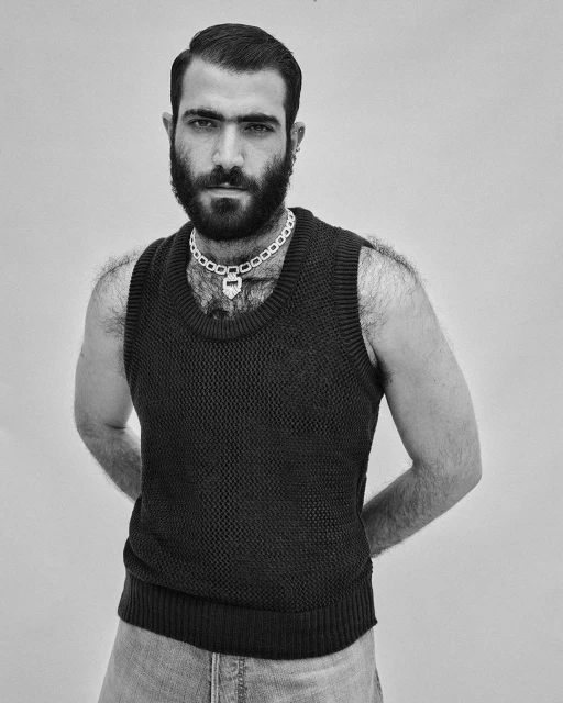 Portrait of an adult man with a beard and a knit vest, posing in a studio. The photo is in black and white, with a simple backdrop.