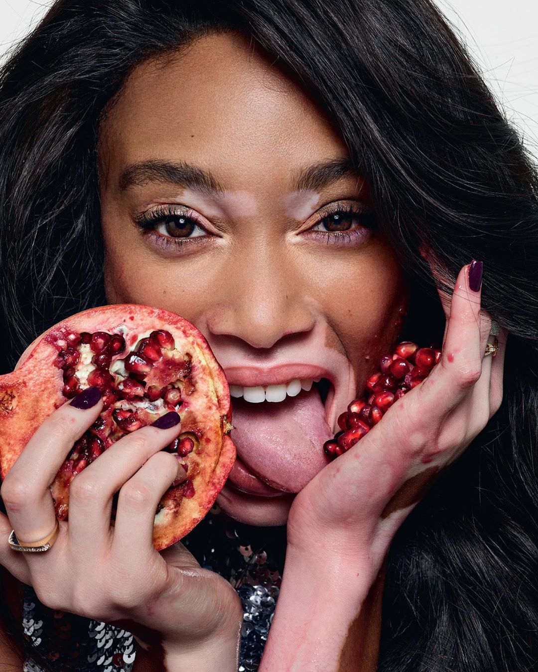 A model poses with a sliced pomegranate, showcasing fresh produce and beauty in a studio setting with a bright, clean backdrop.