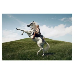 Woman riding a rearing white horse on a lush green hill under a partly cloudy blue sky, photographed by Phil Poynter.