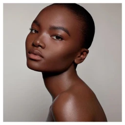 Close-up portrait of a black woman with a shaved head and glowing skin against a neutral grey background