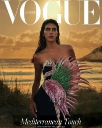 Model in a black strapless dress featuring an ornate beaded flamingo bodice standing against an ocean sunset background.
