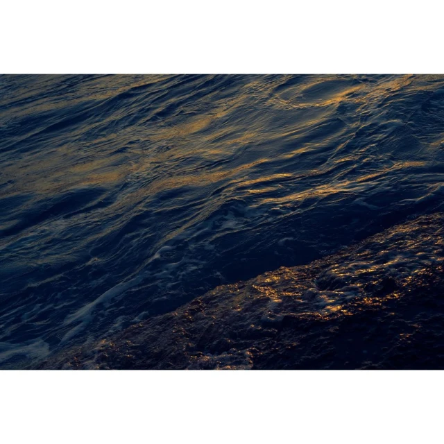 Ocean wave close-up with dark blue water and golden sunlight reflecting on surface, creating a textured and dynamic marine scene.