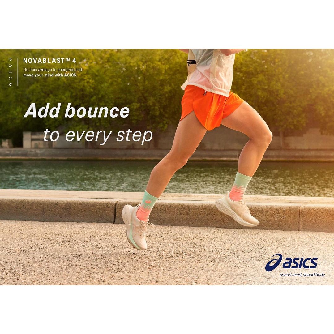 A woman is running on a paved path near a river in athletic apparel and Asics running shoes, on a sunny day.