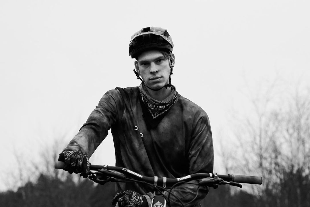 Monochrome portrait of a cyclist with a helmet and bandana, holding the handlebars of a mountain bike outdoors.