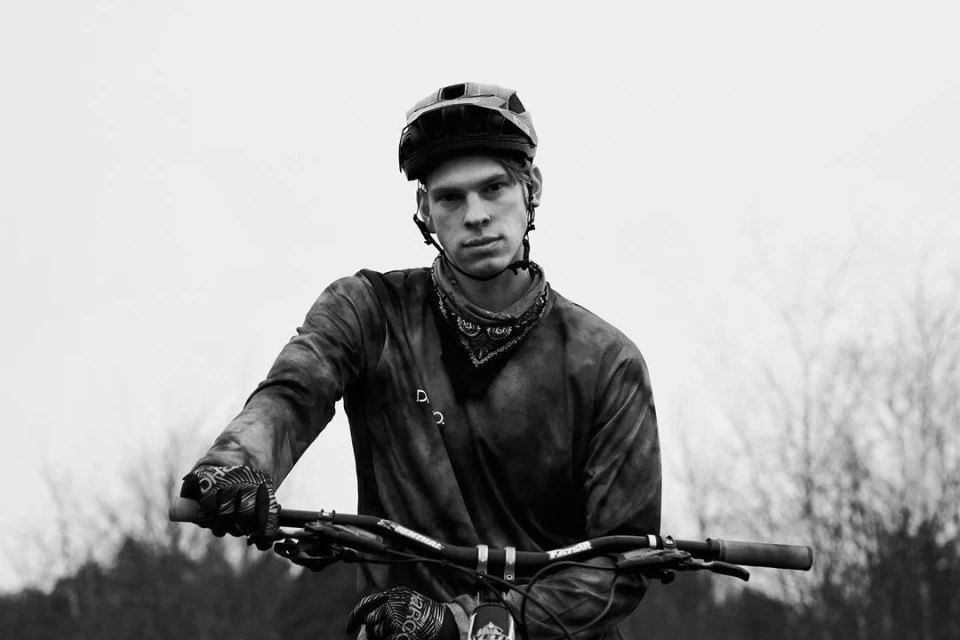 Monochrome portrait of a cyclist with a helmet and bandana, holding the handlebars of a mountain bike outdoors.
