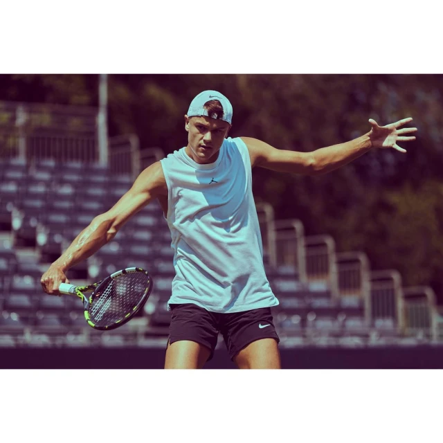 A male tennis player in action on an outdoor court during the daytime. He is wearing athletic wear and holding a tennis racket.