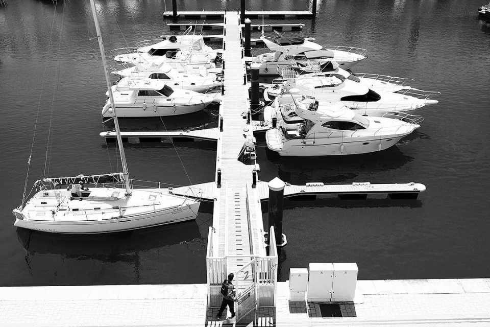 Monochrome aerial shot of docked yachts and a person walking on a pier. The boats are arranged along the pier in an orderly fashion.