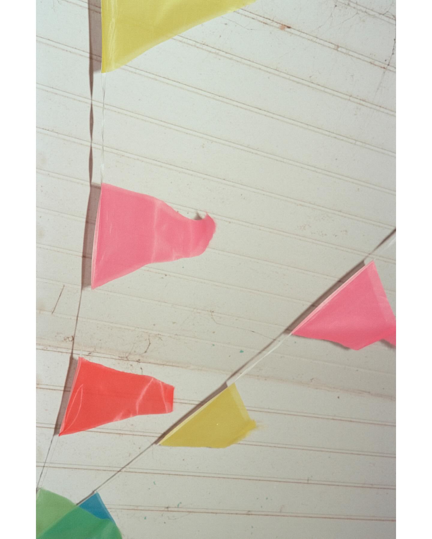 Colorful pennant banner hanging against a white wooden wall or ceiling, creating a festive and decorative atmosphere.