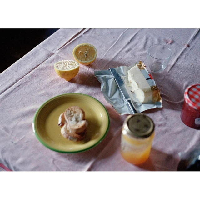 Overhead shot of breakfast foods on a table: sliced lemon, butter, toast on a plate, jars of jelly and honey, and an empty drinking glass.