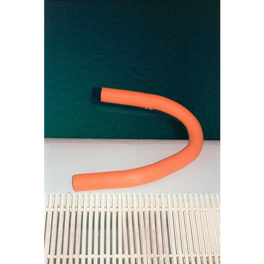 Orange flexible foam exercise bar over a white slatted surface, against a dark green background.