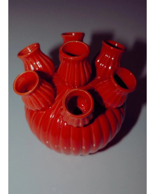 Close-up studio shot of a red ceramic tulipiere, a decorative vase with multiple openings for flower stems, against a gray background.