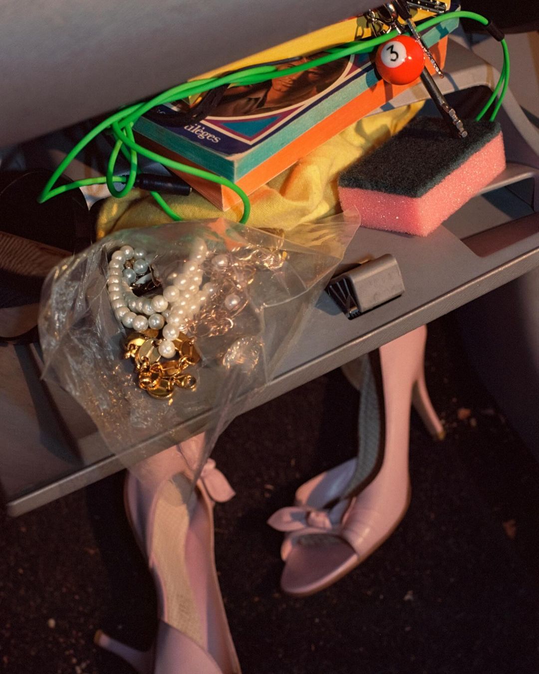 Still life of pink high heels, jewelry, a sponge, and other objects placed in a gray shelf-like structure, captured in a medium shot.