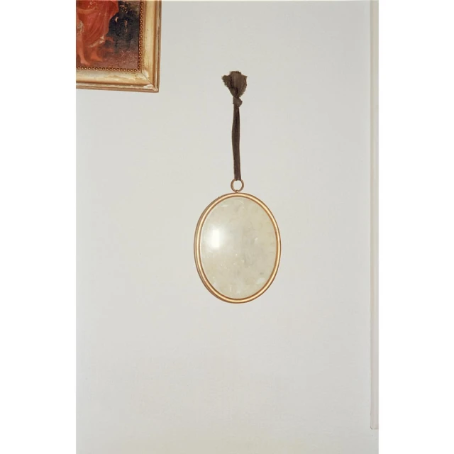 Oval vintage framed decorative mirror hanging on a wall above the floor, with an antique painting on the white wall in the background.