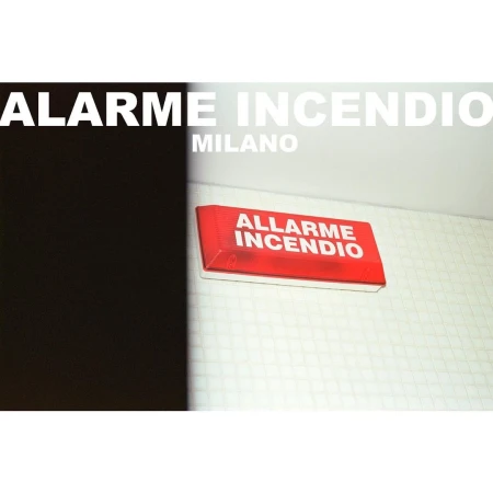 A red fire alarm box with white text is mounted on a white wall, with a partially visible black element to the left.