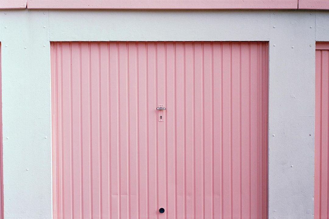 Light pink garage doors with white trim on concrete facade, creating a symmetrical, pastel architectural pattern.