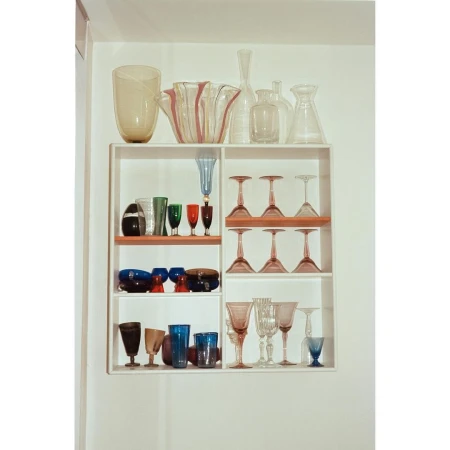 Display cabinet with decorative glass vases and drinking glasses in a variety of shapes and colors, creating a colorful and elegant display.